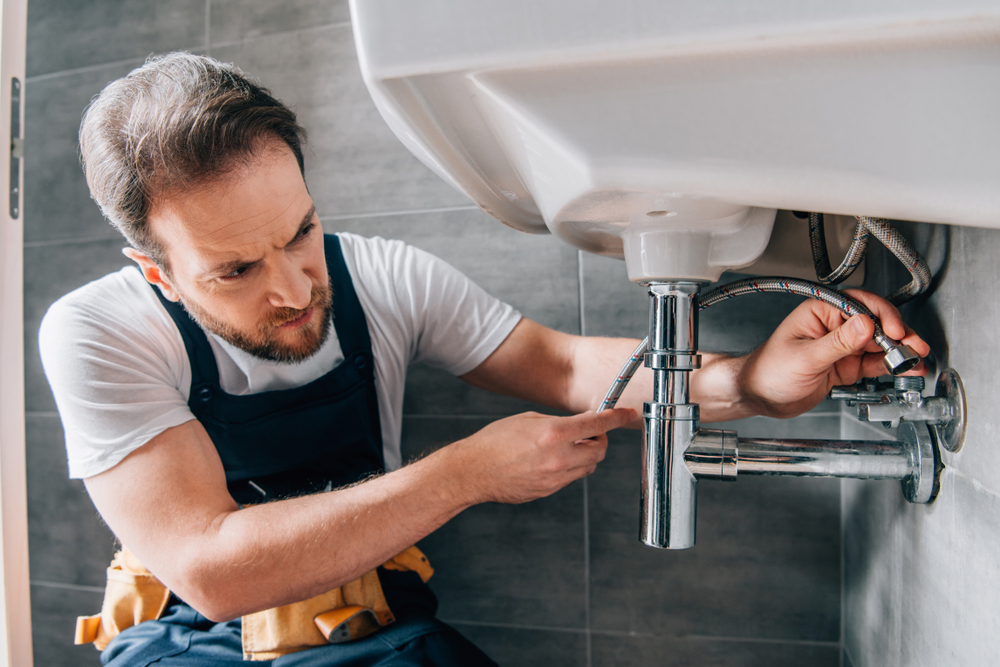 Plumber repairing pipework under a basin